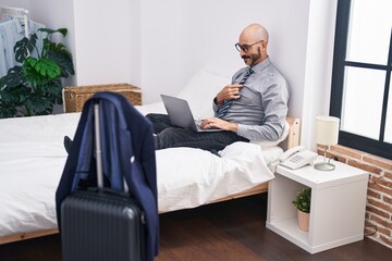 Young hispanic man business worker using laptop sitting on bed at hotel room