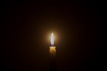 A single burning candle flame or light glowing on a spiral white candle on black or dark background...