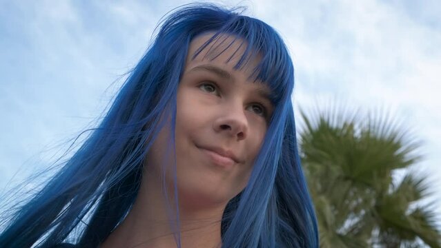 Girl with dyed blue hair on beach. A smiling girl with dyed hair style pas her time on summer beach. A concept of modern relaxation on beach.