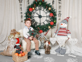Portrait of a sitting smiling 4 year old boy in a Christmas and New Year interior with a large wall...