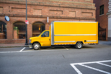 Small yellow rig semi truck with long box trailer standing on the city street making local...