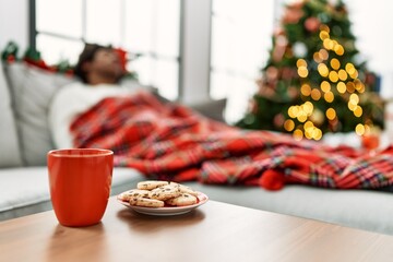 Young african american man sleeping lying on the sofa by christmas tree at home.