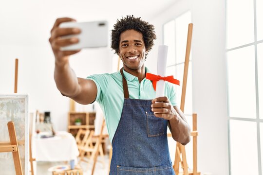 Young african american artist man holding diploma make selfie by the smartphone at art studio.
