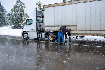 Truck driver puts chains on the wheels of the big rig semi truck with semi trailer to drive safely...