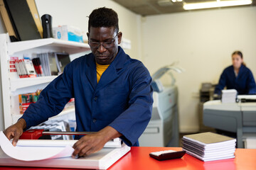 Serious print shop worker cuts paper on a professional cutter