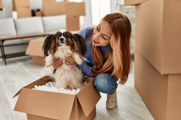 Young caucasian woman sitting on floor holding dog of cardboard box at new home