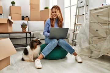 Young caucasian woman using laptop sitting with dog at new home