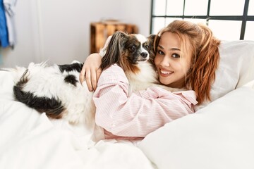Young caucasian woman lying on bed hugging dog at bedroom