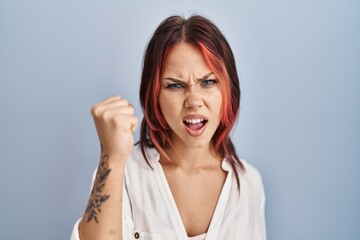 Young caucasian woman wearing casual white shirt over isolated background angry and mad raising fist frustrated and furious while shouting with anger. rage and aggressive concept.