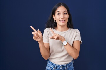 Young hispanic woman standing over blue background pointing aside worried and nervous with both hands, concerned and surprised expression