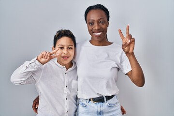 Young mother and son standing together over white background smiling with happy face winking at the...
