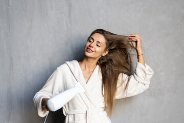Young woman using hair dryer near mirror at home