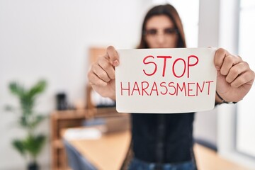 Young beautiful hispanic woman business worker holding stop harassment message banner at office