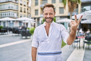 Middle age man outdoor at the city showing and pointing up with fingers number two while smiling confident and happy.