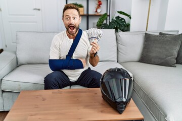 Fototapeta premium Middle age man with beard wearing arm on sling for motorbike accident holding insurance money celebrating crazy and amazed for success with open eyes screaming excited.