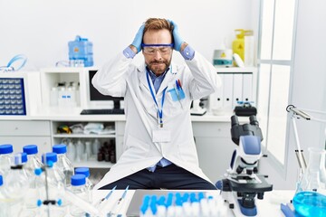 Middle age man working at scientist laboratory suffering from headache desperate and stressed because pain and migraine. hands on head.