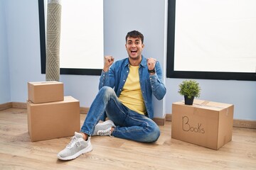 Young hispanic man sitting on the floor at new home celebrating surprised and amazed for success with arms raised and open eyes. winner concept.