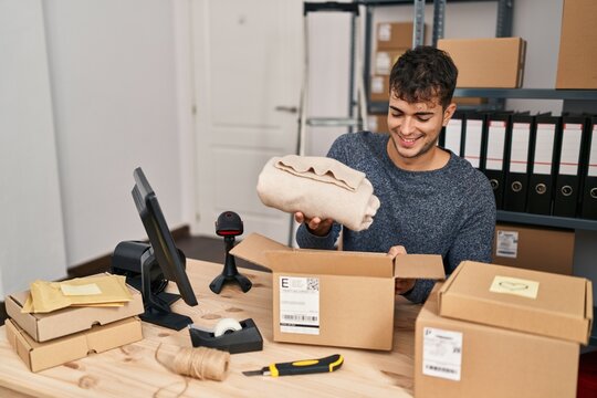 Young hispanic man ecommerce business worker preparing clothes package at office
