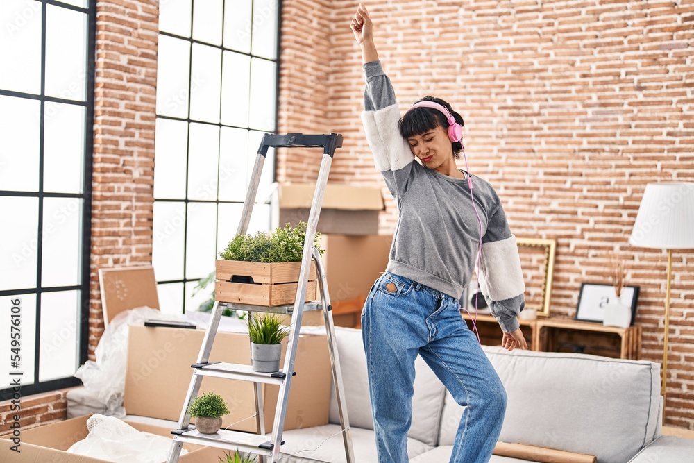 Sticker Young woman listening to music and dancing on sofa at new home