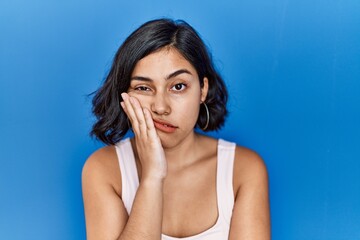 Young hispanic woman standing over blue background thinking looking tired and bored with depression problems with crossed arms.
