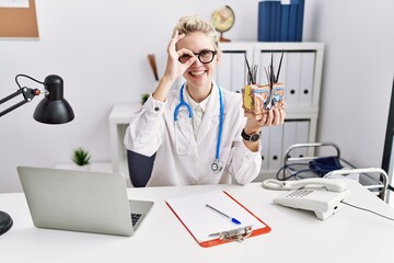 Young doctor woman holding model of human anatomical skin and hair at the clinic smiling happy...