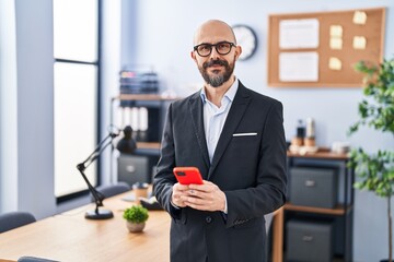 Young bald man business worker smiling confident using smartphone at office