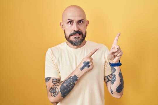 Hispanic man with tattoos standing over yellow background pointing aside worried and nervous with both hands, concerned and surprised expression