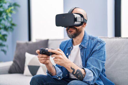 Young bald man playing video game using virtual reality glasses at home