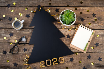 Fototapeta na wymiar New Year background. Blackboard Christmas tree 2023 New Year on wooden table. New Year composition desk with coffee, notebook, festive decor. New Year resolutions 2023, goals, planning concept