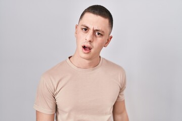 Obraz premium Young man standing over isolated background in shock face, looking skeptical and sarcastic, surprised with open mouth