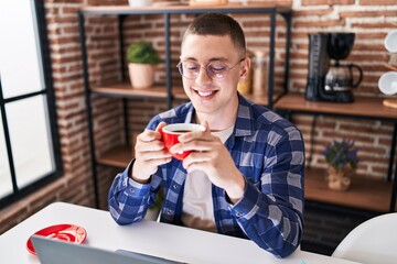 Young hispanic man drinking coffee sitting on table studying at home