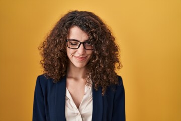 Hispanic woman with curly hair standing over yellow background winking looking at the camera with sexy expression, cheerful and happy face.