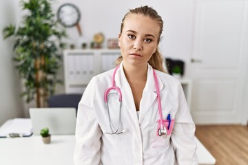 Young caucasian woman wearing doctor uniform and stethoscope at the clinic relaxed with serious expression on face. simple and natural looking at the camera.