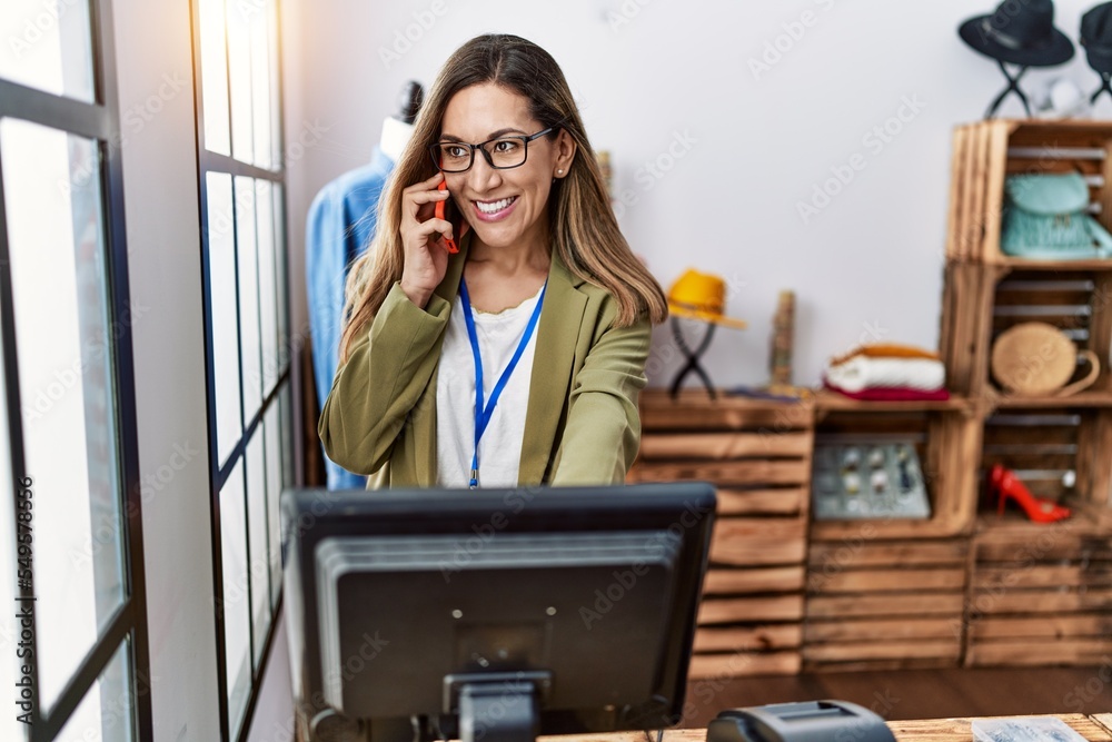 Canvas Prints Young hispanic woman talking on the smartphone working at clothing store