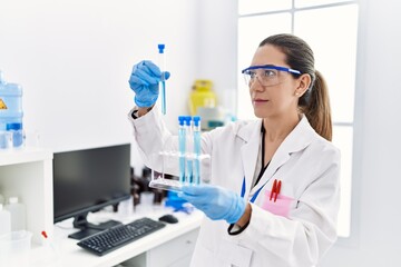 Fototapeta premium Young hispanic woman wearing scientist uniform holding test tube at laboratory