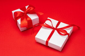 Close up shot of two gift boxes wrapped in white paper and decorated with ribbon bows isolated over bright colored red background