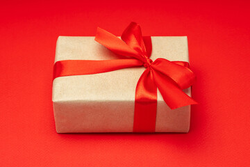Close up shot of gift box wrapped in craft paper and decorated with satin ribbon bow, isolated on red background