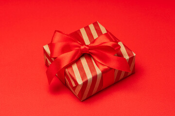 Close up shot of gift box wrapped in striped kraft paper and decorated with satin ribbon bow, isolated on red background