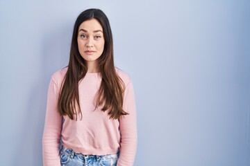 Obraz premium Young brunette woman standing over blue background relaxed with serious expression on face. simple and natural looking at the camera.