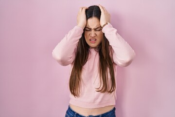 Young brunette woman standing over pink background suffering from headache desperate and stressed because pain and migraine. hands on head.