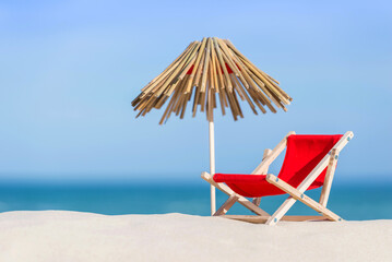 Concept of a sun lounger and a thatched umbrella on a beautiful beach, ocean on the background