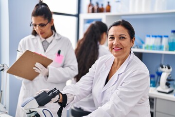 Fototapeta premium Three woman scientists using microscope write on checklist at laboratory