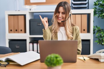 Young hispanic woman wearing call center agent headset working at the office smiling happy pointing with hand and finger to the side