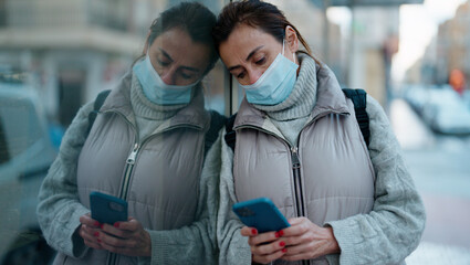 Middle age hispanic woman wearing medical mask using smartphone at street