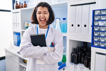 Young hispanic woman working at scientist laboratory celebrating crazy and amazed for success with open eyes screaming excited.
