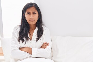 Young beautiful hispanic woman sitting on bed with unhappy expression and arms crossed gesture at bedroom