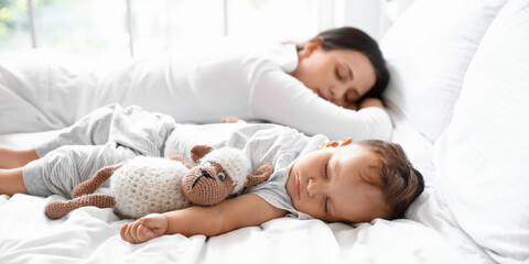 Adorable baby with toy and mother sleeping on bed