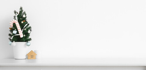 Small Christmas tree with candle on table near light wall