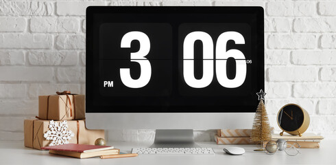 Computer monitor with Christmas presents and stationery on table near white brick wall