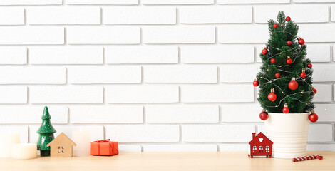 Small Christmas tree with decor and candles on table near white brick wall